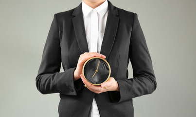 Woman holding alarm clock on grey background. Time management concept