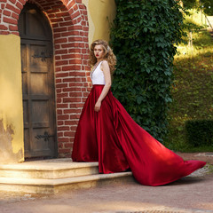 Young beautiful woman in white and red evening dress standing and posing close to yellow red brick...