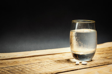 glass of cold water and pills for a hangover on a wooden table