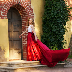 Young beautiful woman in white and red evening dress standing and posing close to yellow red brick...