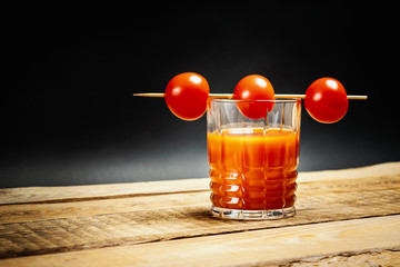 juicy red bloody mary drink with tomatoes on a stick on a wooden table