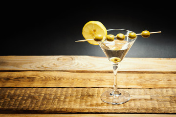 delicious martini drink in a glass with olives on a stick and lemon on a wooden table