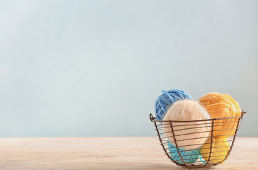 Basket with knitting yarn on table against color background