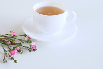 Floral composition made of beautiful pink roses on white wooden background with a cup of tea. Feminine office desk, styled stock image, flat lay, top view . Empty space for your text.