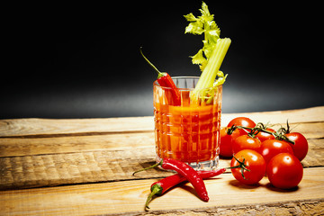 juicy red drink bloody mary with a piece of green celery and chilli peppers and tomatoes on a wooden table