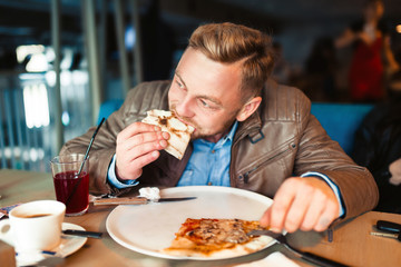 Leisure, people and holidays concept. Young man eating piece of pizza   at restaurant
