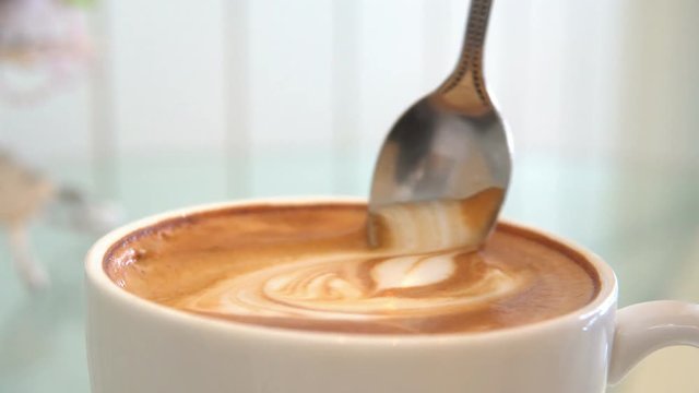 Close up. Coffee Stiring milk foam in a cup of latte coffee. 4K Resolution