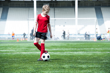 Full length portrait of  teenage boy leading ball while playing football during practice in outdoor stadium, copy space