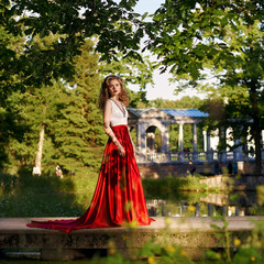 Fashion style photo of young beautiful woman in evening dress with white top and red flying skirt...