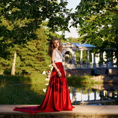 Fashion style photo of young beautiful woman in evening dress with white top and red flying skirt...