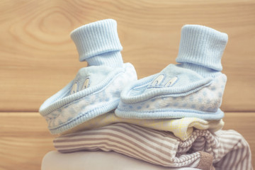 blue booties on clothes stack. Pastel clothes for baby infant on wooden background. Newborn.