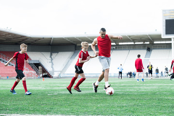 Full length portrait of Latin-American football coach teaching junior team of teenage boys in outdoor stadium, copy space