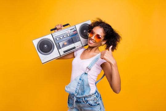 Yes, done! Portrait of trendy stylish girl in eyewear holding boom box on shoulder gesturing thumb up sign looking at camera isolated on yellow background. Recommend choice advice concept