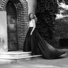 Young beautiful woman in white and red evening dress standing and posing close to yellow red brick...