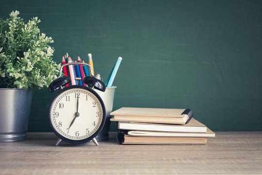 Alarm clock on wooden table on blackboard background in classroom,back to school concept