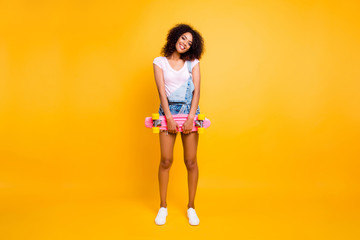 Full size portrait of funky cute coquette holding pink skate board in hands looking at camera isolated on yellow background. Urban outside outdoor street style concept