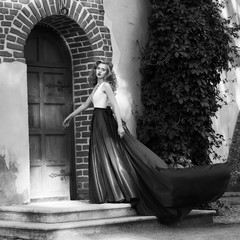 Young beautiful woman in white and red evening dress standing and posing close to yellow red brick...