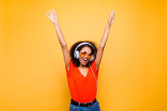 Portrait of cheerful positive chic holding raised arms having headphones on head listening music singing song enjoying weekend vacation isolated on yellow background