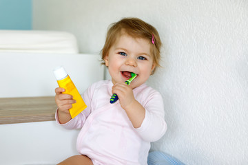Little baby girl holding toothbrush and brushing first teeth. Toddler learning to clean milk tooth.