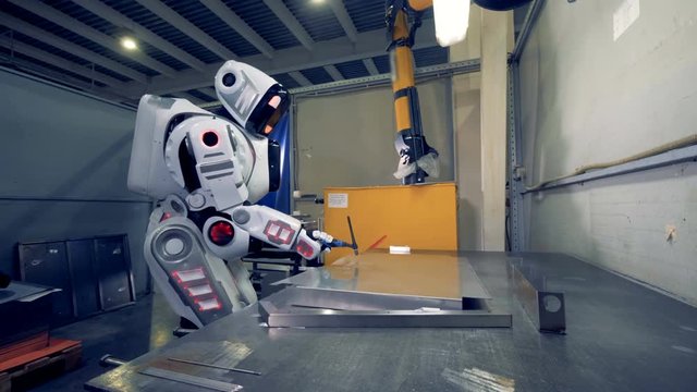 Factory robot is working with welding equipment and a metal sheet at a plant.