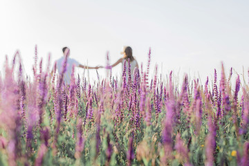 Cute young couple in love is holding their hands in a field of flowers