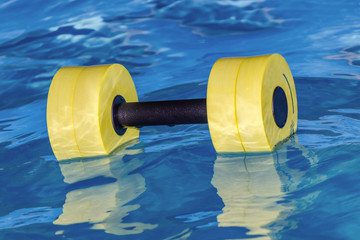 A yellow dumbbell for water aerobics lies in the water. Sport.