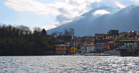 Obraz premium Cloudy blue sky with mountains and old small village with colorful buildings on lake Mergozzo in Piemont, Italy
