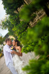 The groom dressed in white kissing a beautiful bride. Wedding couple kissing in the middle of green plants in the Park