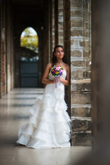 The bride in the gallery of stone walls in a beautiful white wedding dress with a bouquet of flowers