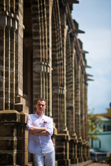 The groom in a white shirt posing near the stone columns of the Catholic Church