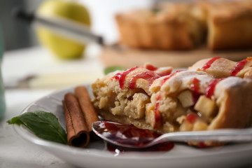 Plate with piece of tasty homemade apple pie and raspberry jam on table