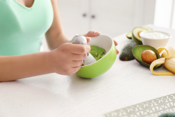 Woman making nourishing mask with avocado in kitchen
