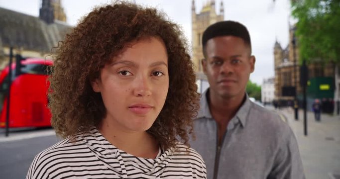 Portrait of black male and female standing on London street with red bus, African American couple in the city smiling at camera, 4k