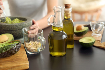 Ingredients for homemade avocado mask on kitchen table and blurred woman on background