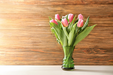 Vase with beautiful tulips on table against wooden background