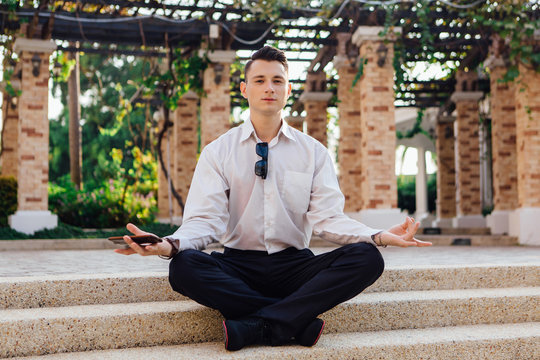 Young businessman sitting on stairs outdoors in lotus pose