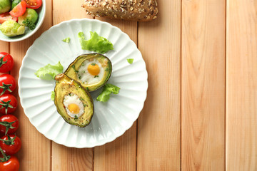 Baked avocados with eggs and vegetables on wooden background