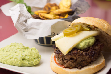Delicious beef burger with plantain chips and guacamole on a newspaper