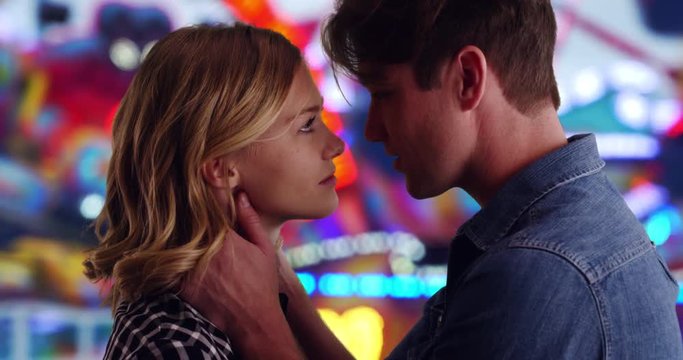 Caucasian man and woman gaze into each other's eyes then kiss, Loving young couple kissing at the county fair, 4k