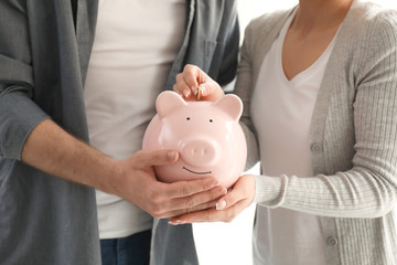 Couple putting coin into piggy bank, closeup. Money savings concept