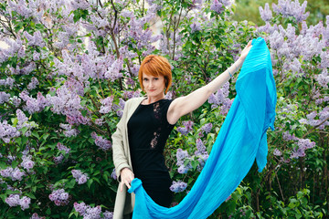 Amazing red henna hair girl in black dress and bright coat with big blue shawl posing in bushes of...