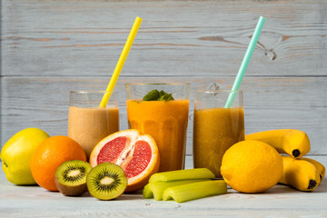 Three glasses of smoothies with straws and various fresh fruits