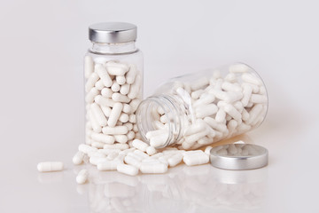 Fototapeta na wymiar White soft gelatin capsules in transparent glass bottles with some scattered pils isolated on white background. Medical drug tablet for illness and pain treatment: painkiller, aspirin, antibiotic