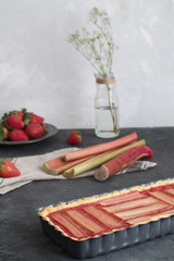 Fototapeta na wymiar Scene with fresh baked rhubarb cake and fresh rhubarb and strawberries on the background
