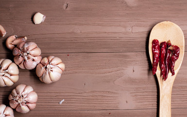 The garlic head put at the left side and wooden spoon with dried pepper put at the right side,on grunge surface timber board.