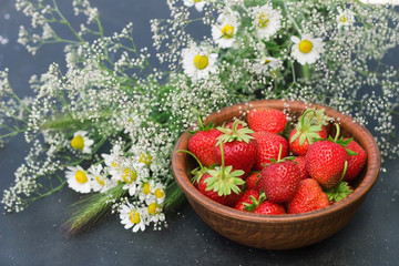 red strawberry in a clay cup with flowers gypsophila daisy field on a dark background