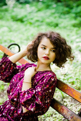 Naklejka premium A wonderful girl in a purple dress, sitting on a bench in the park