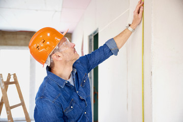 Handyman using a tape measure while working on construction site. Repairman wearing safety hardhat and protective eye goggles. 