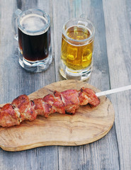 Beer and snack to beer. Light and dark beer in glasses and a shish kebab on a skewer on a wooden board.