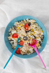 A baby blue bowl with cold rice salad with two spoons.